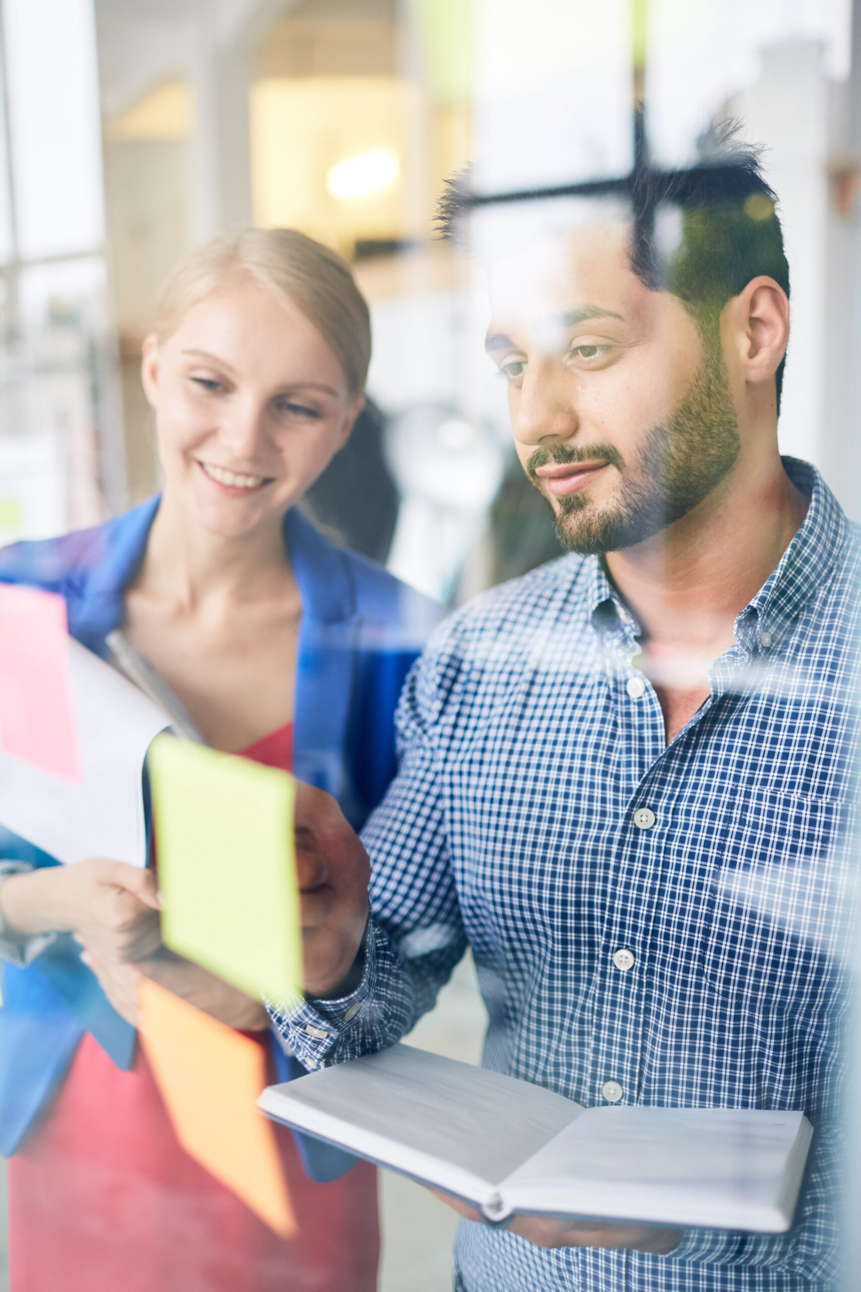 Two young managers discussing one of reminders on notepaper at the beginning of working day